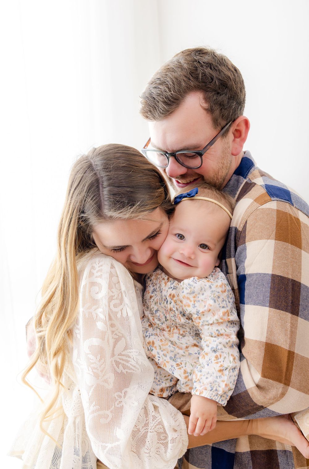 Family wearing neutral colors embraces together in a series of tender candid moments against white background.