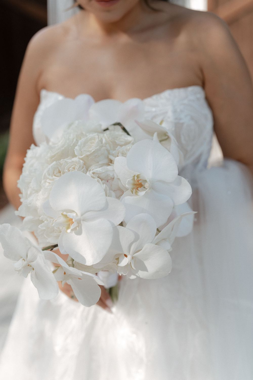Close-up detail of white orchids adorning a strapless wedding dress bodice in natural light.