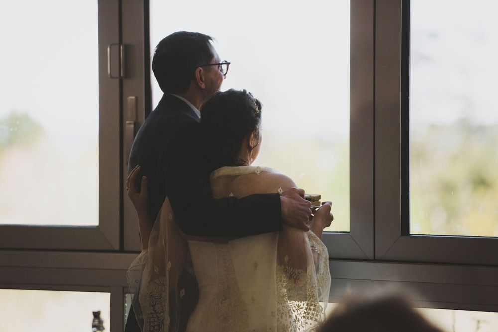 Couple embracing while looking out large windows during wedding reception.