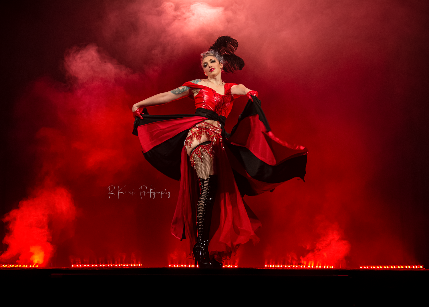 Dramatic performance on stage with dancer in red costume amid smoke effects.