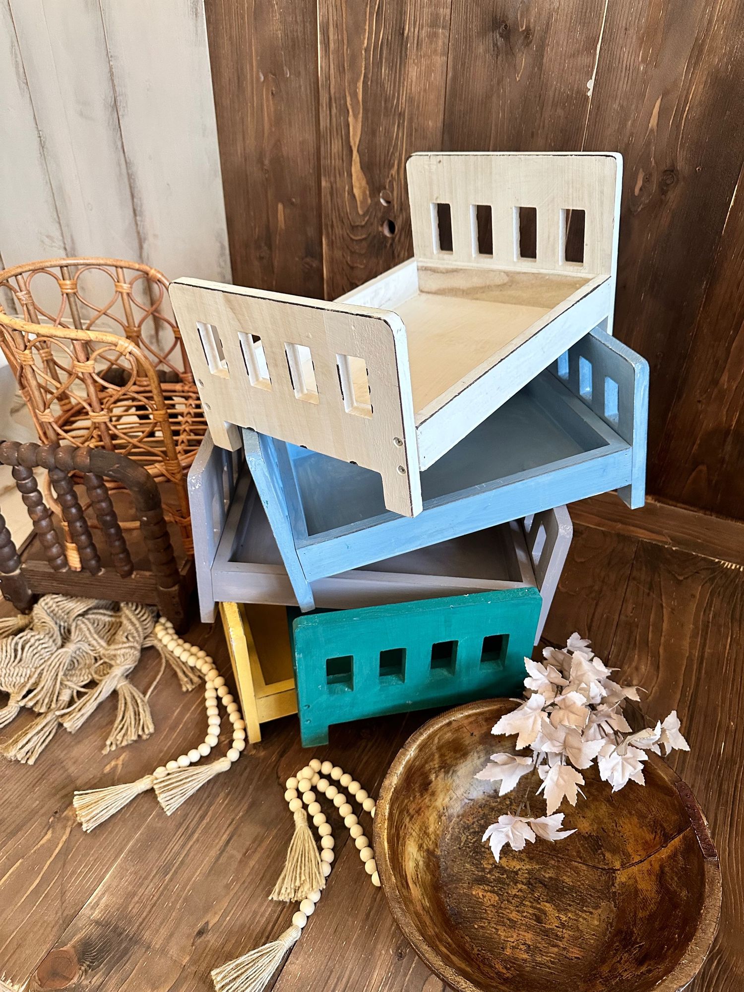 Stacked wooden toy beds in different pastel colors with rustic decor elements.