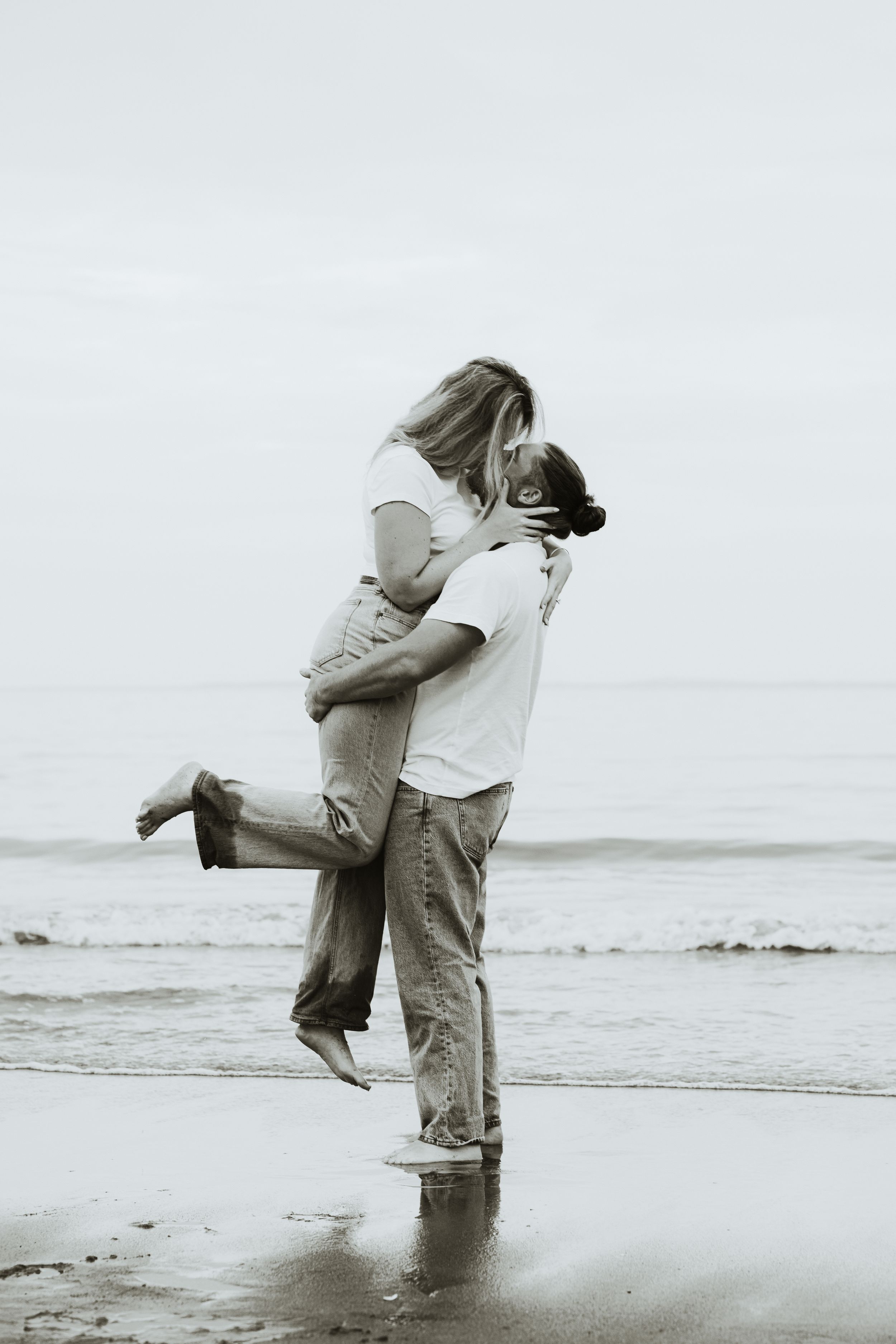 Couple embracing on a beach, man lifting woman in a romantic black and white coastal photo.