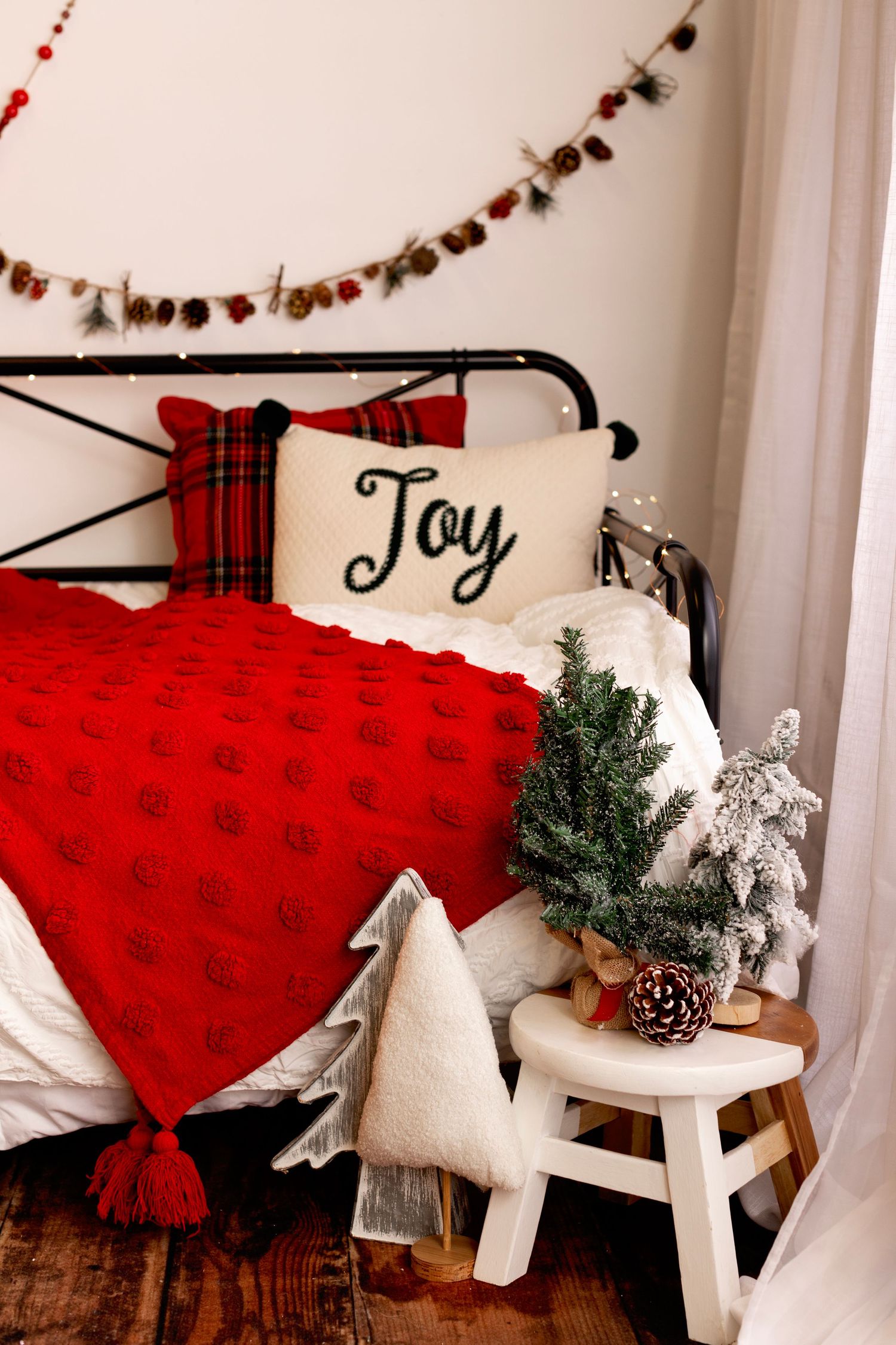 Cozy Christmas bedroom corner with red plaid blanket, Joy pillow and mini trees.