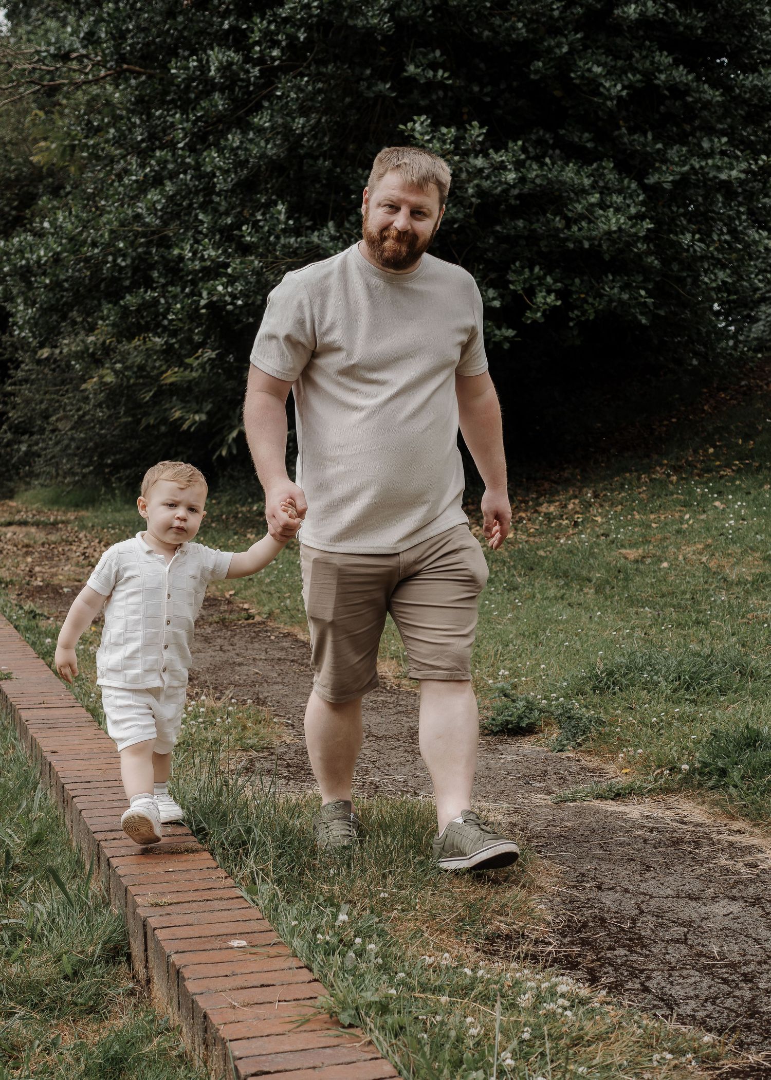 Family Photoshoot - People walk along a brick-lined path through a garden setting.