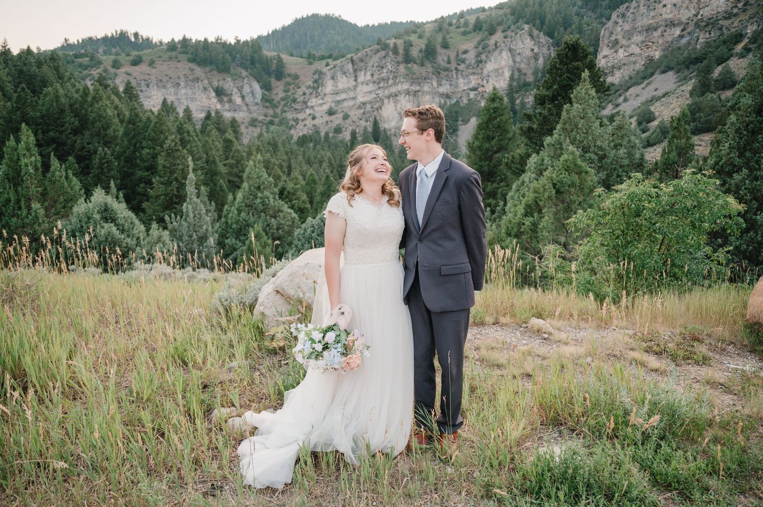 Newlyweds share a romantic moment in front of majestic mountain cliffs.