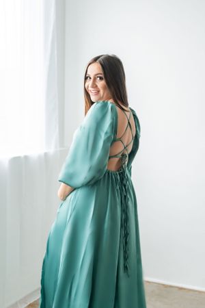 An elegant teal dress with open back detail photographed against a white wall.