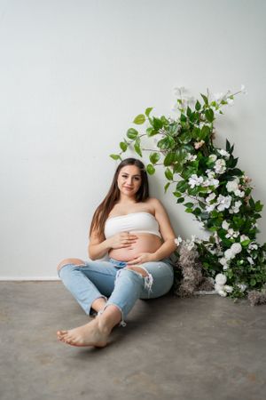 A casual maternity portrait with white floral backdrop and distressed jeans.