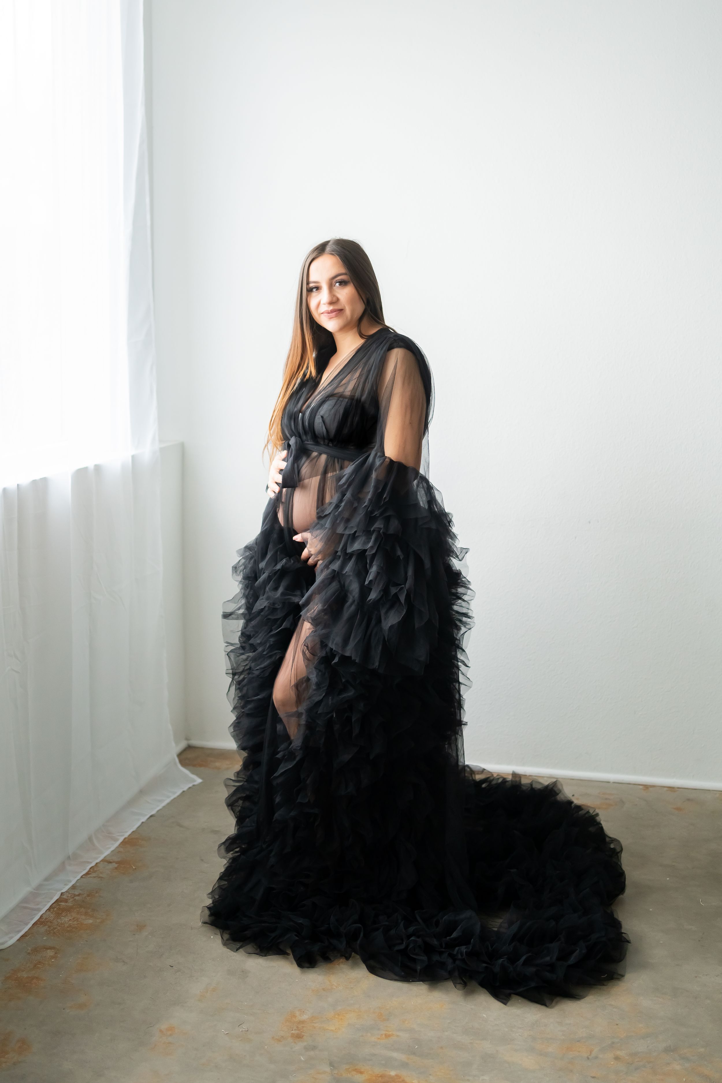 Dramatic black tulle maternity gown in a minimalist white studio setting.