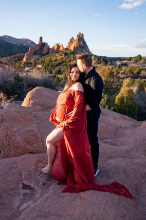 Couple poses romantically on red rocks with mountain formations in background.