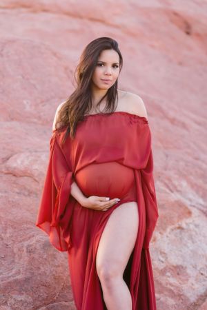 Maternity photo of woman in flowing red dress against red rock formations.