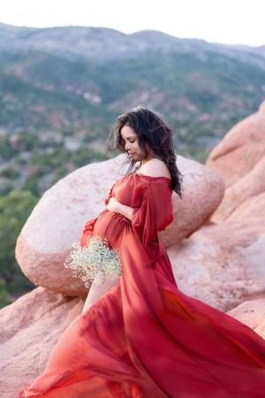 Woman in red dress holds baby's breath flowers against dramatic red rock landscape.