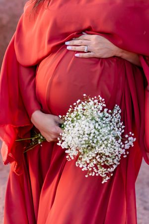 Maternity photo showing pregnant belly in flowing red dress with white baby's breath flowers.
