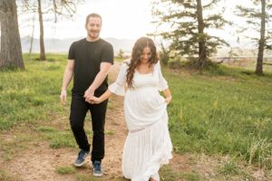 Couple walks together on grassy path with pine trees in background during evening light.