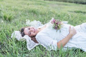 A person in a white dress lies in a grassy meadow holding a bouquet of wildflowers.