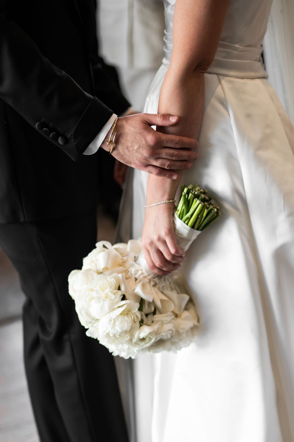 Intimate wedding detail shot of hands holding a white rose bouquet.
