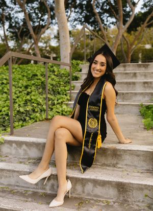 Graduate in cap and gown poses confidently on concrete steps.
