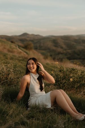 Joyful outdoor portrait session in white dress among wildflowers at sunset for graduation and senior photos in Orange County