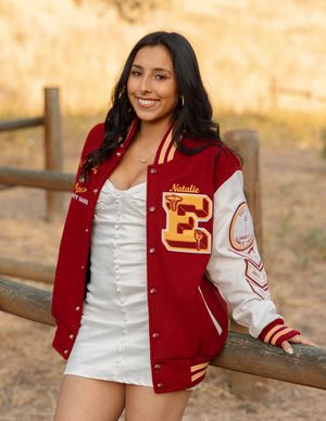 A person wearing a red and white varsity letterman jacket poses by a wooden fence for graduation and senior photos in Orange County