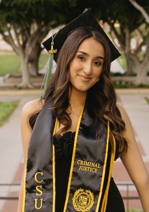 Criminal Justice graduate wearing academic regalia smiles at camera.