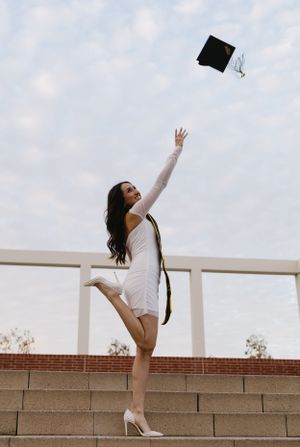 Graduate in white dress tosses graduation cap in celebratory pose.