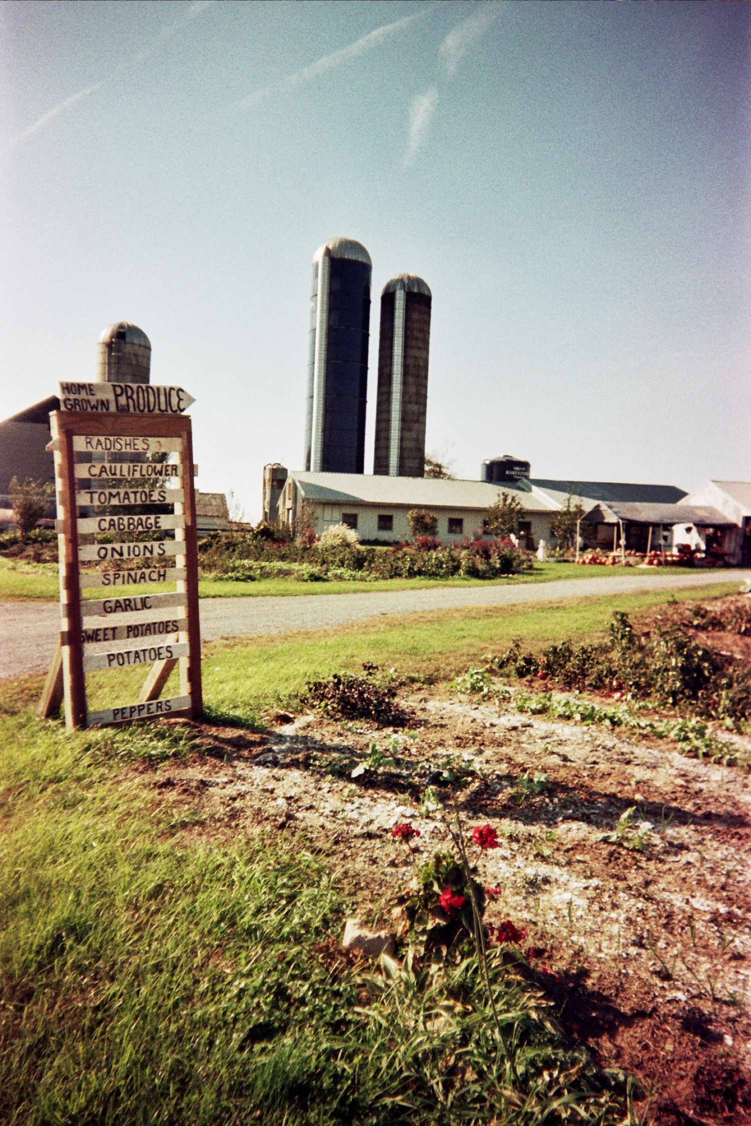 farm stand sign post with silos and garden in background