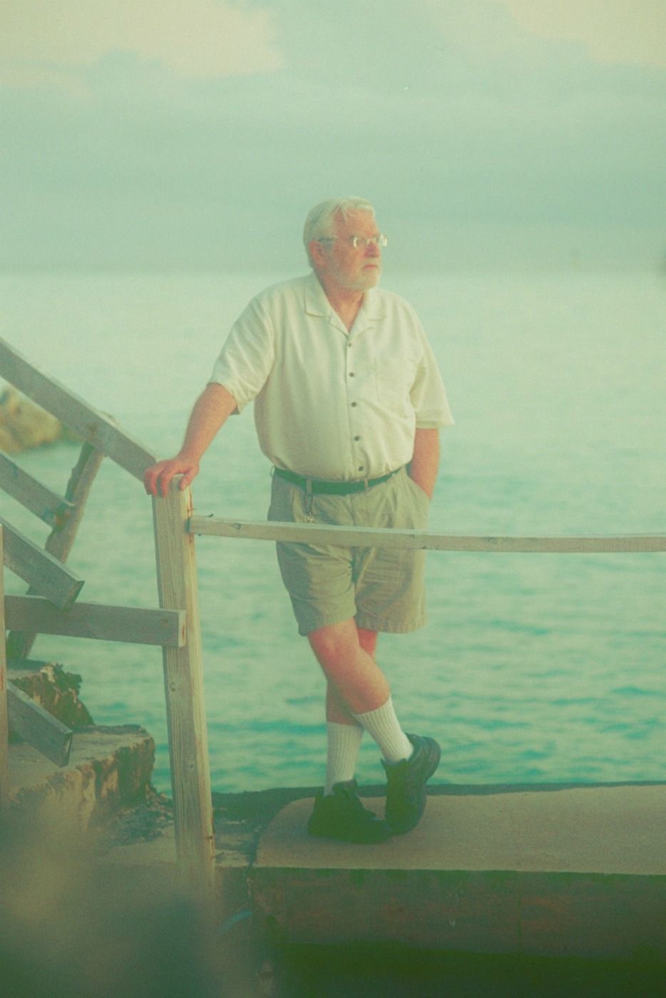 older man leans against rickety dock, looking out at water