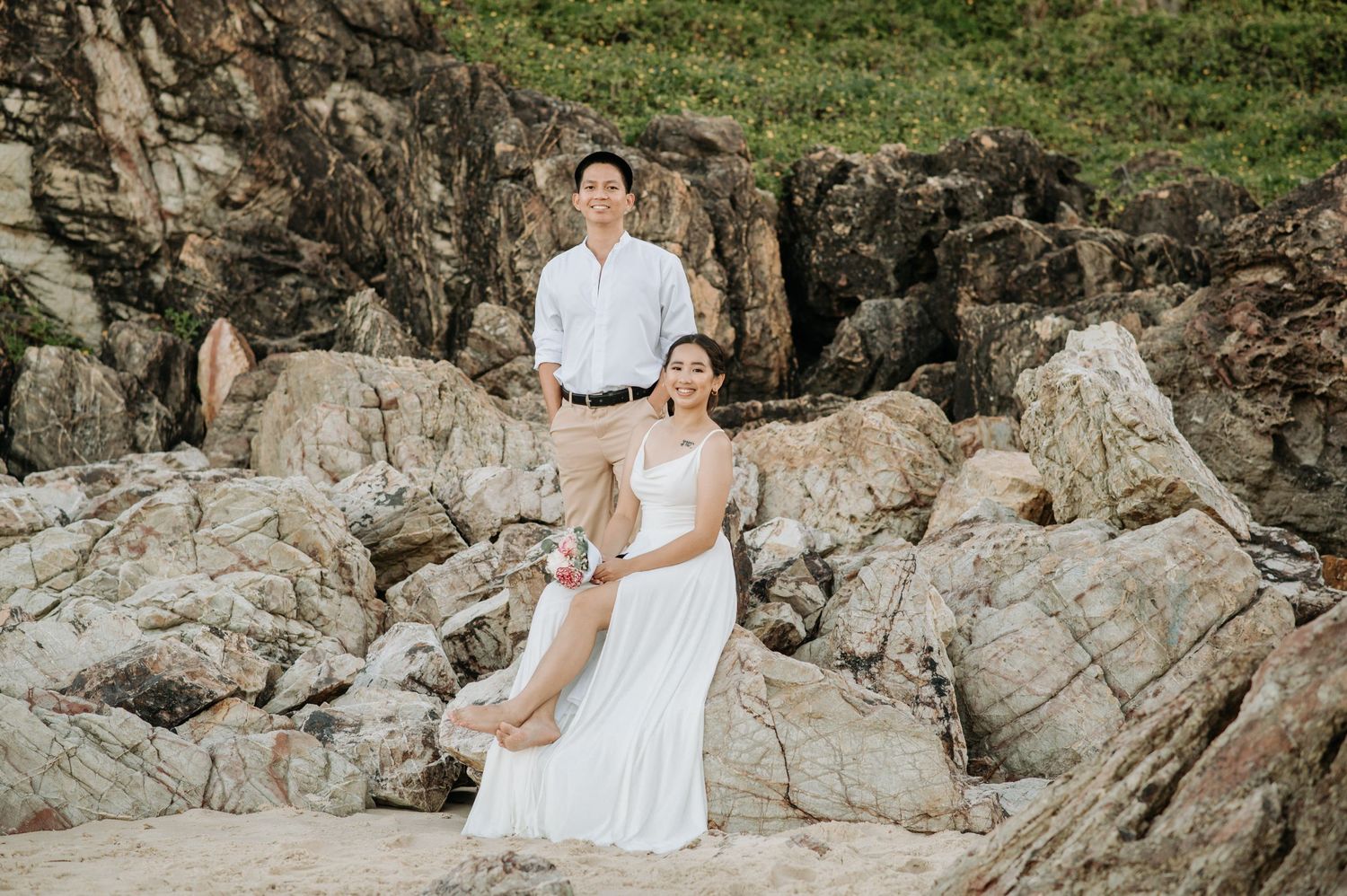 A romantic photoshoot on rocky coastal cliffs with a couple in wedding attire.