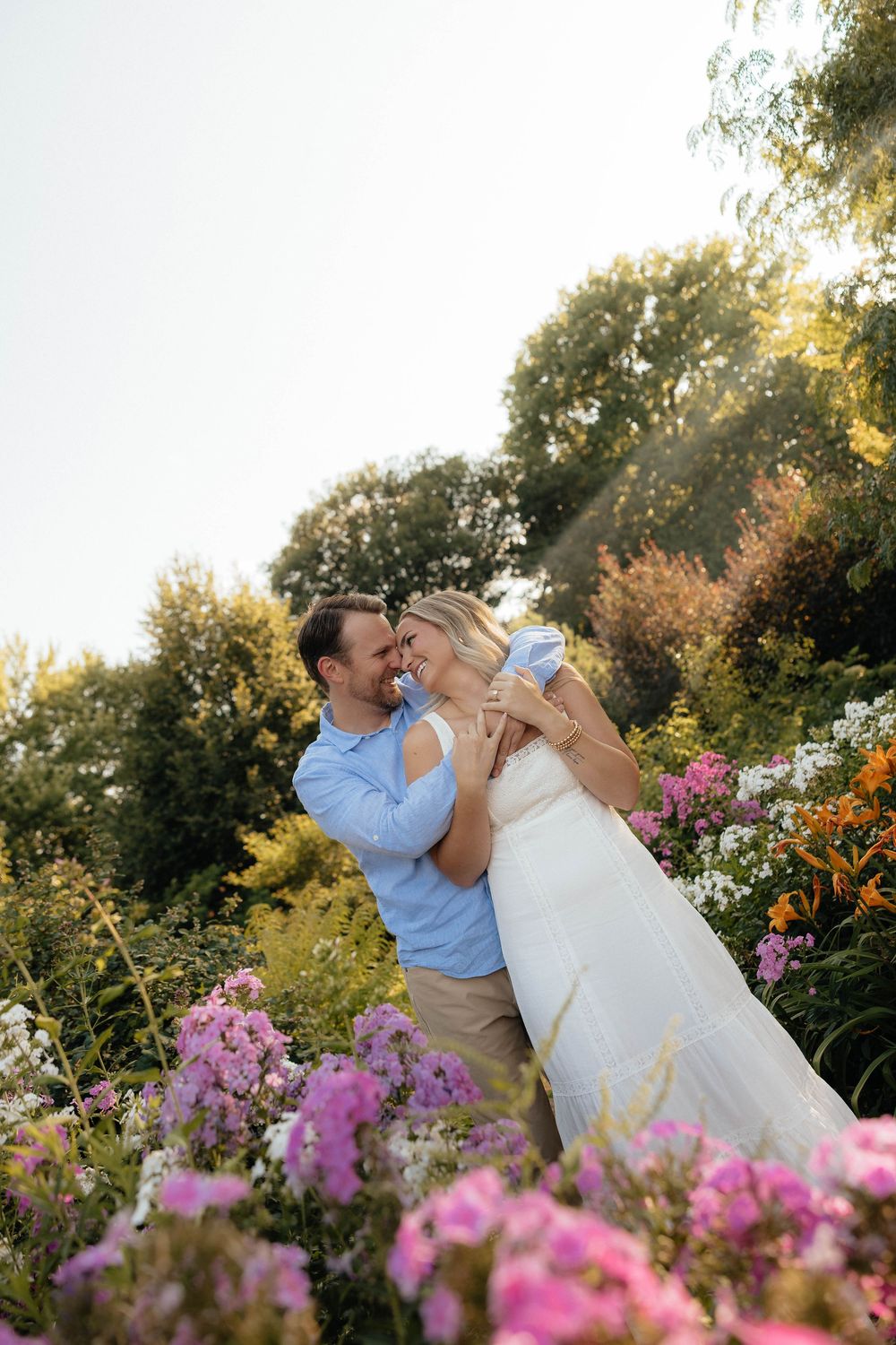 Couple embracing and laughing together surrounded by colorful garden flowers at sunset.