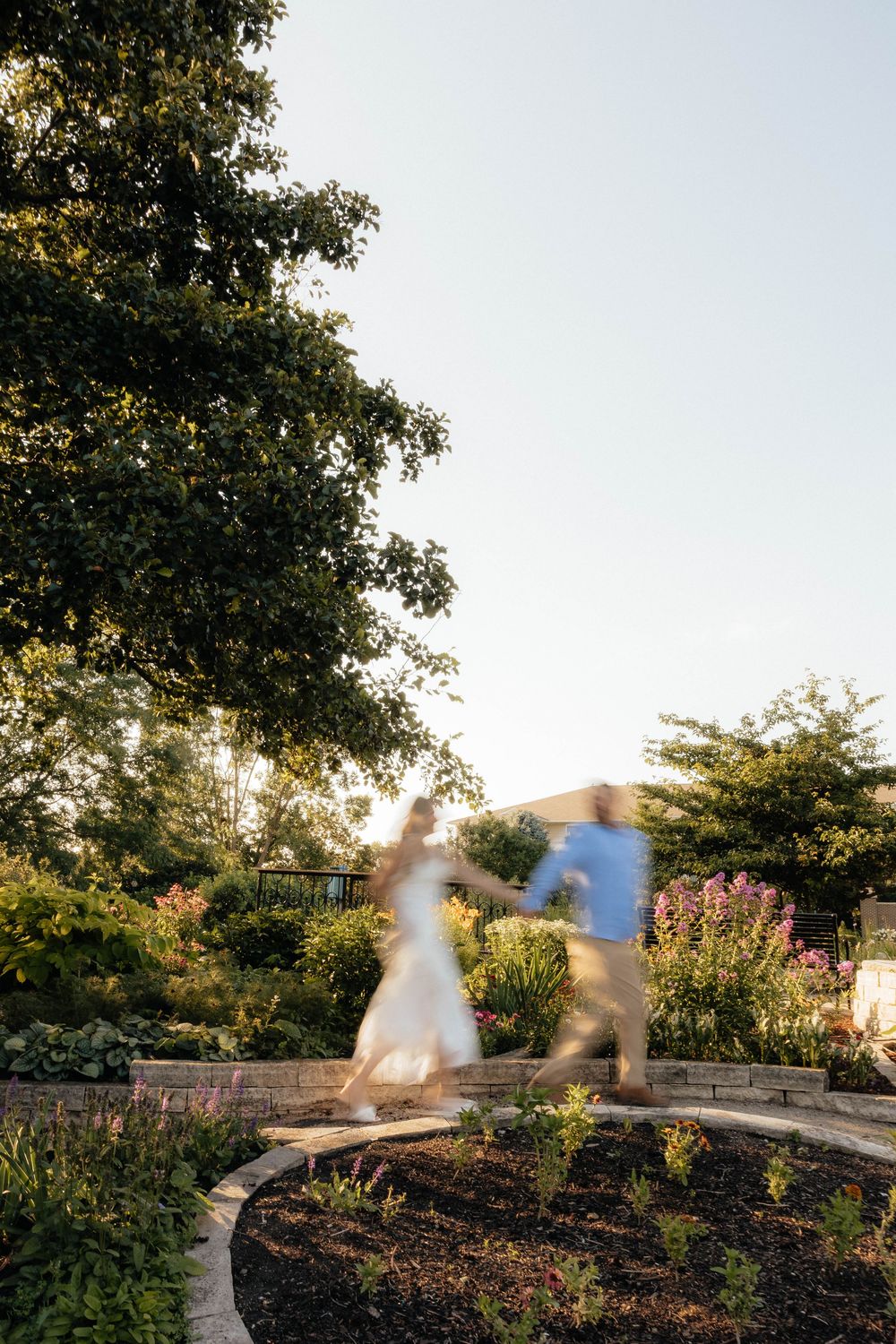 Blurred couple holding hands walking through a lush garden at golden hour.