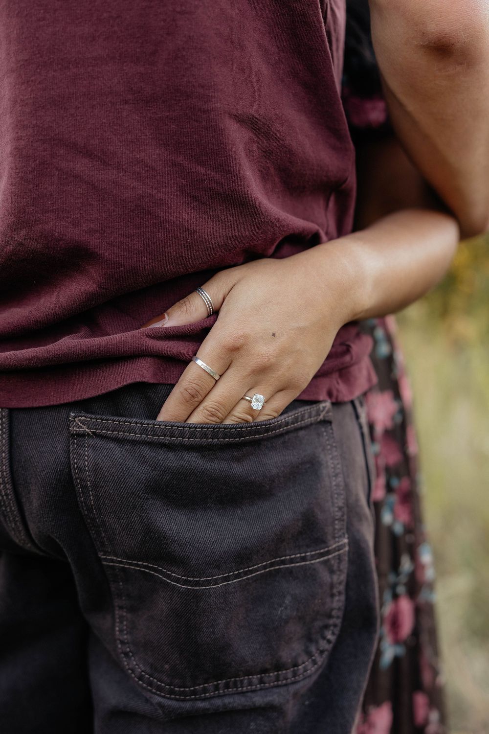 Close-up view of a hand with engagement ring resting in the back pocket of dark denim jeans.