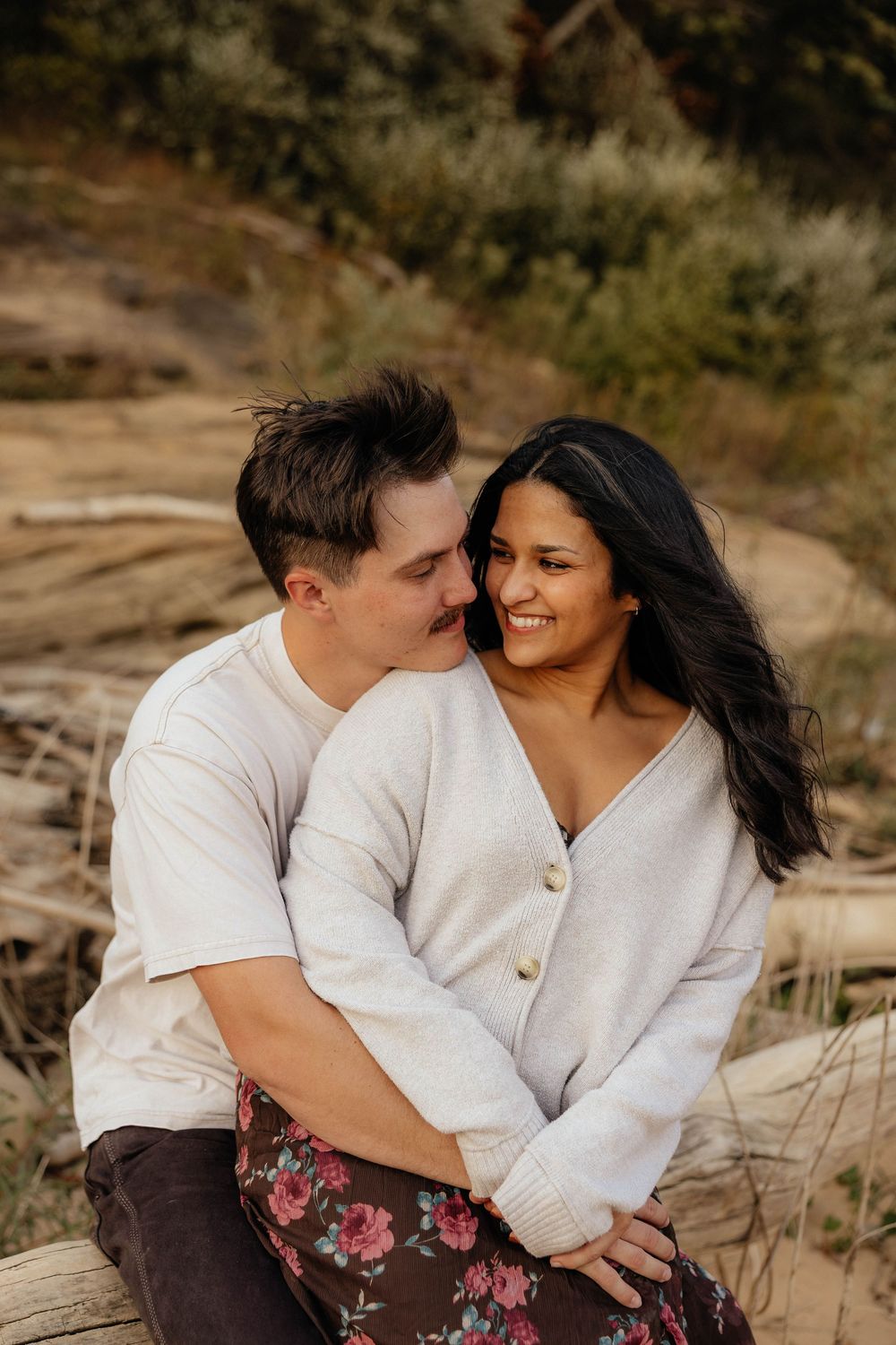 A couple shares an intimate moment while sitting together on rocky terrain during golden hour.