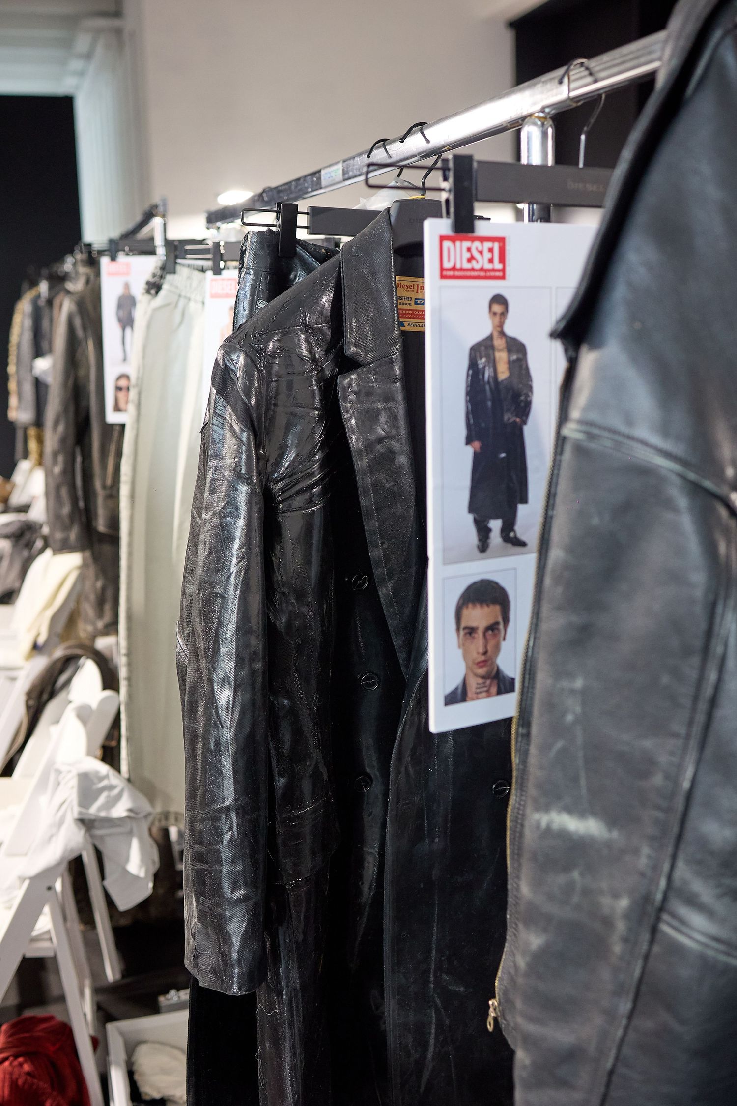 Clothing rack backstage at a fashion show with leather garments and model casting cards.