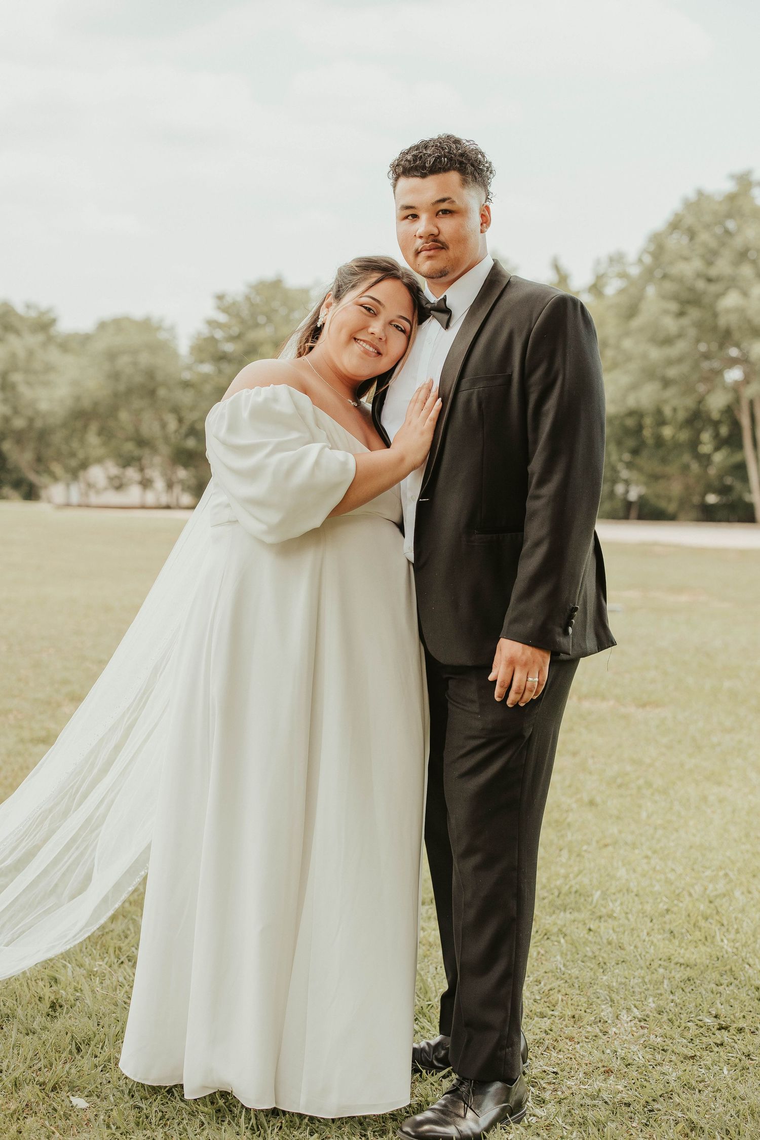 A happy couple poses together outdoors in elegant wedding attire on their special day.