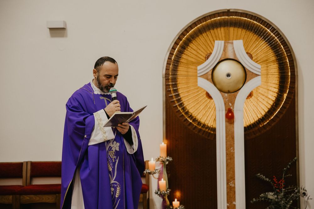 A priest in purple vestments reads from a book during a church service.