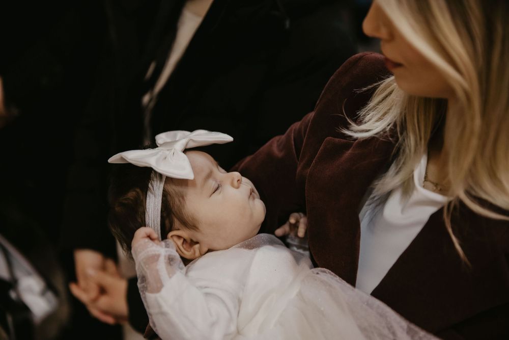 A small infant wearing white clothing and a bow during a baptism ceremony.