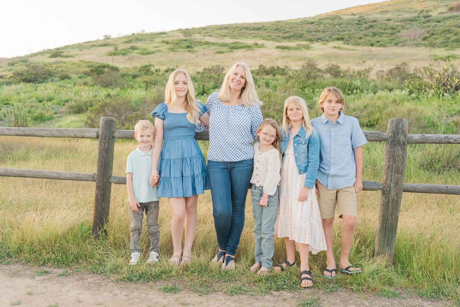 Group of people in coordinated blue and white outfits standing together by a rustic wooden fence in a scenic meadow.