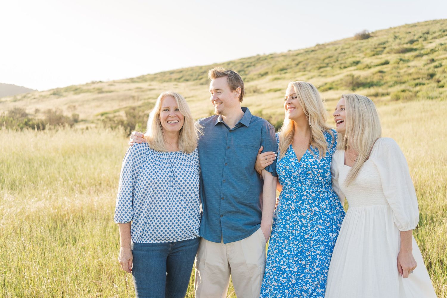 A group of four people stands together smiling in a golden grassy field on a sunny day.
