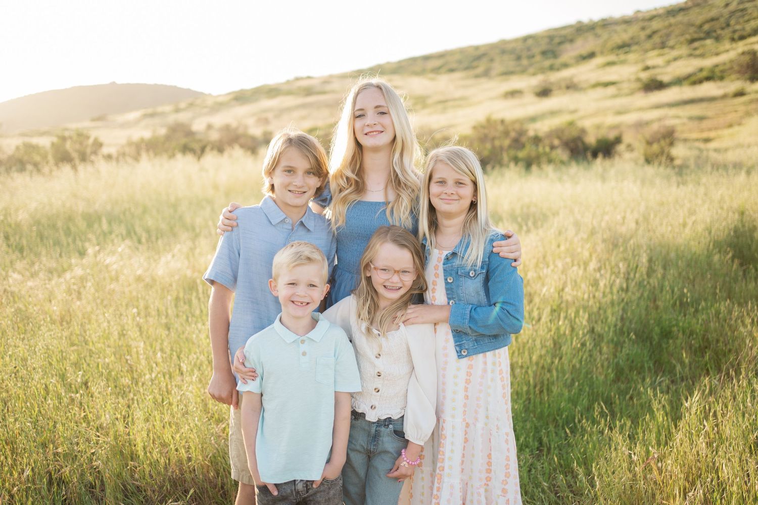 A group portrait in a sunlit grassy field with golden light creating a warm, natural backdrop in the mountains.