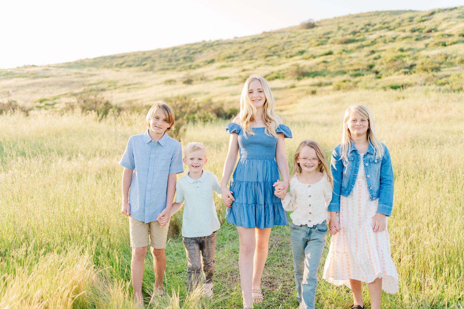 A family stands together in a golden grassy field on a hillside during sunset.
