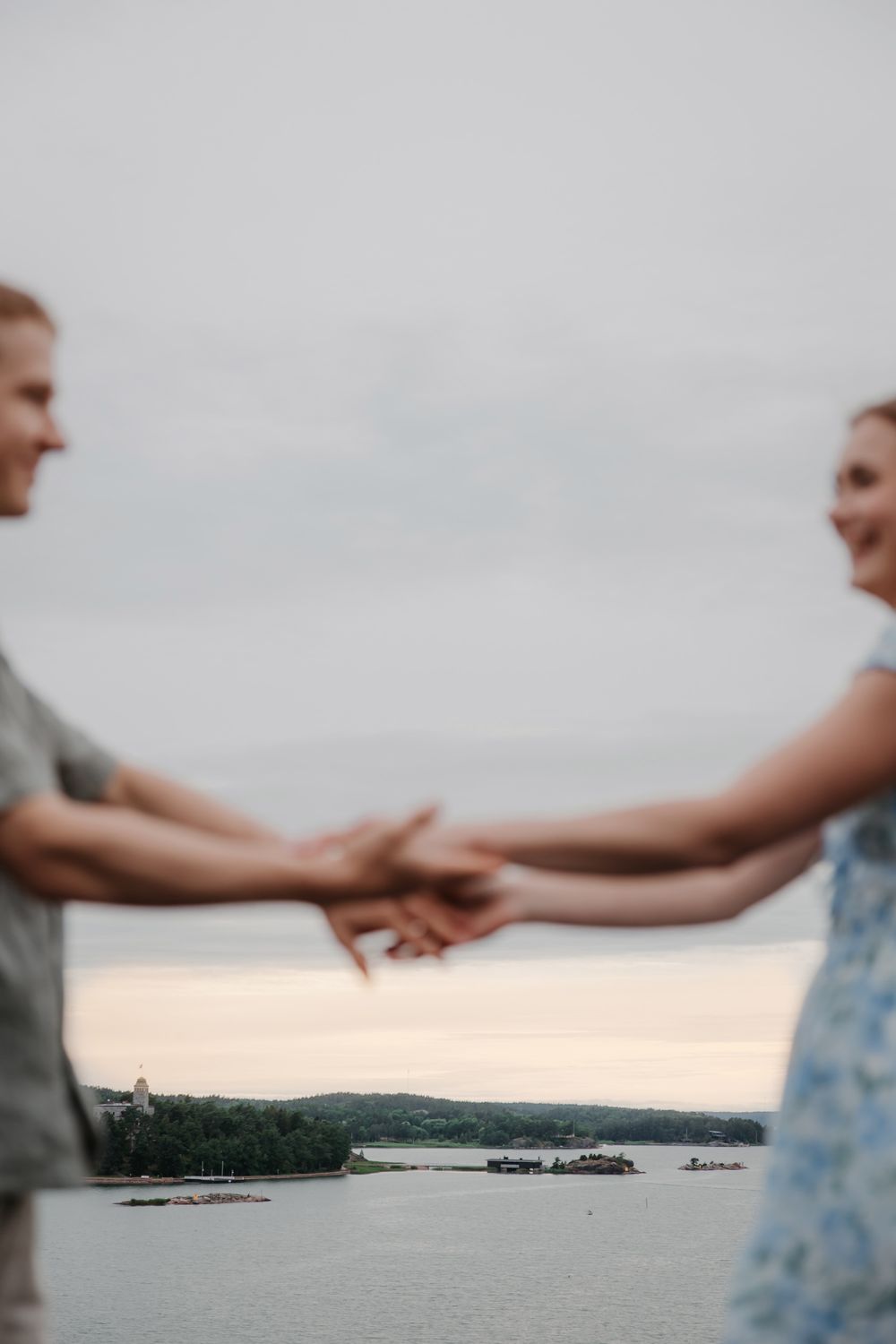 Two people holding hands against a serene waterfront landscape at dusk.