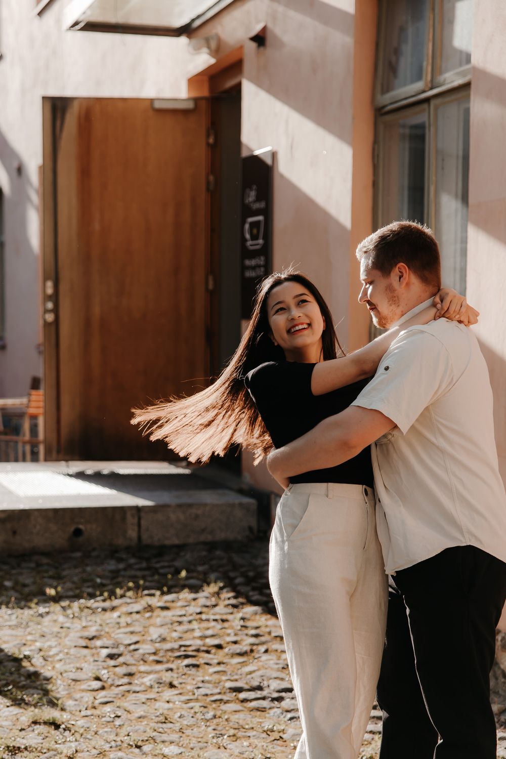 Playful couple spinning and dancing together during outdoor photoshoot.