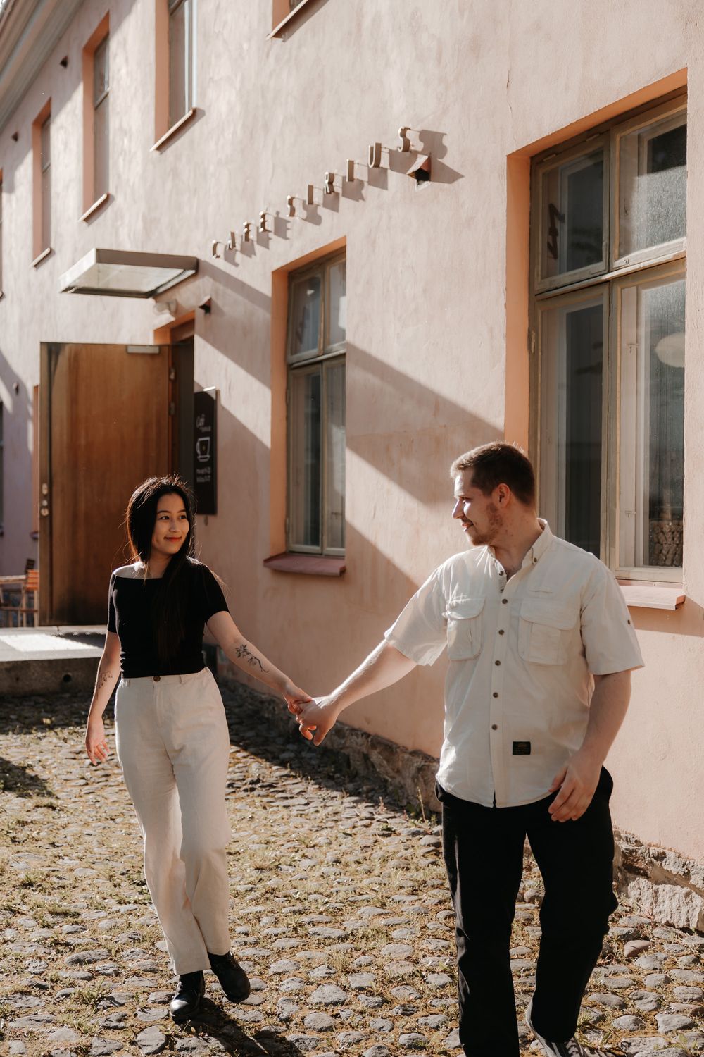 Couple holding hands and dancing in sunlit courtyard during romantic photo session.