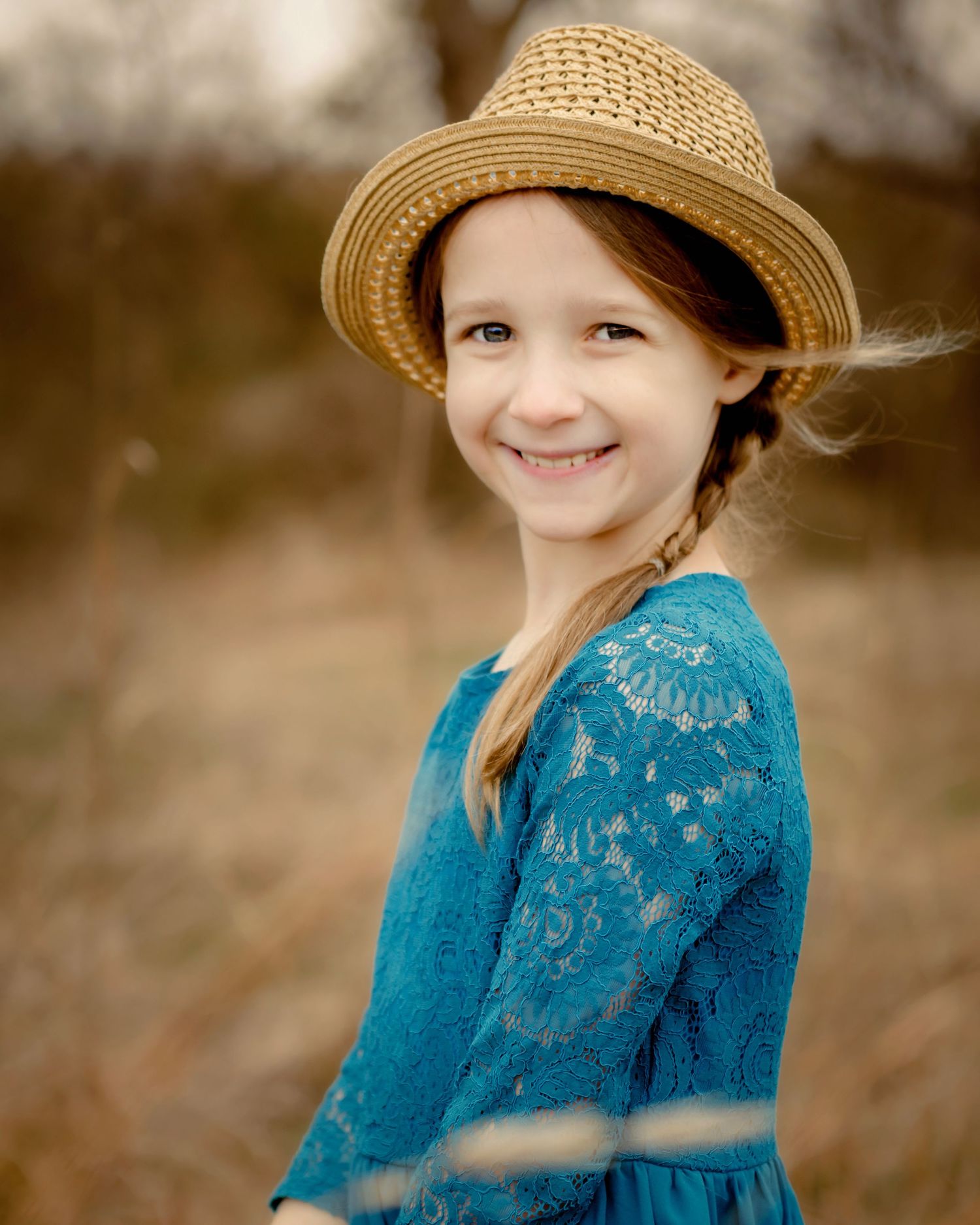 Young child in a blue dress and straw hat smiling during Keller, Texas family portraits.