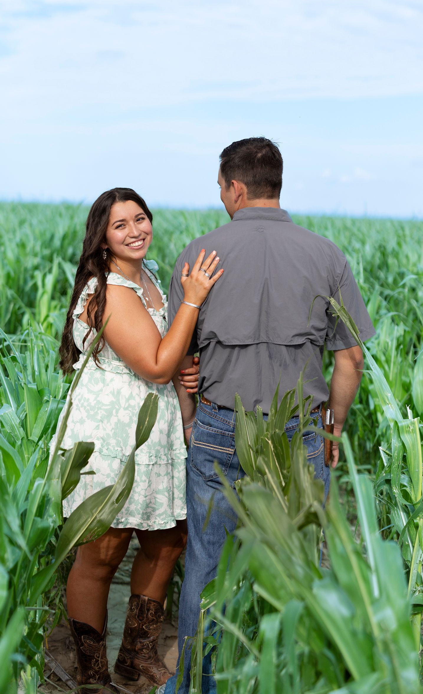 Playful couple walking through a lush green cornfield on a sunny day.