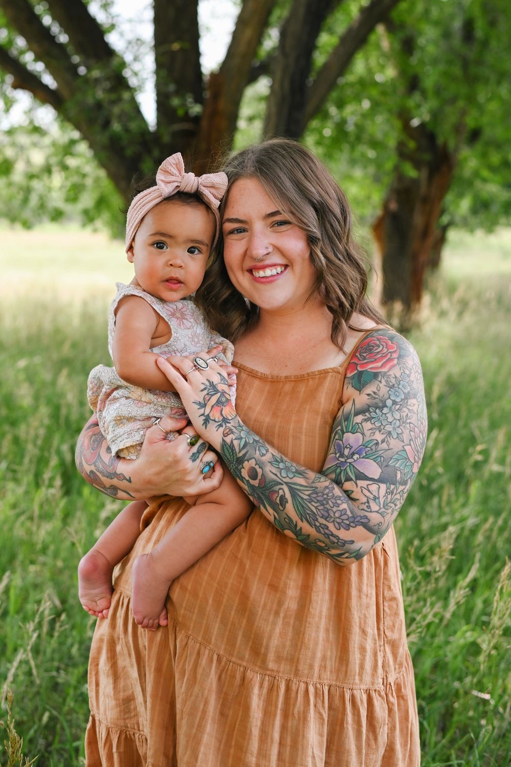 Outdoor portrait in a grassy field with trees, featuring a sleeveless orange dress and decorative tattoo sleeve.