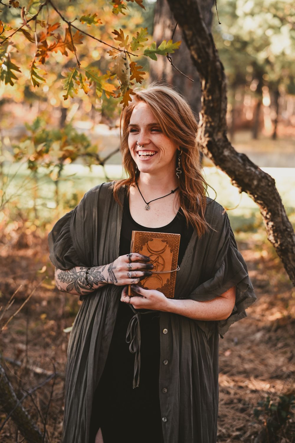 A person in a dark sweater holds a coffee mug while enjoying an autumn day under golden-leaved trees in a park.