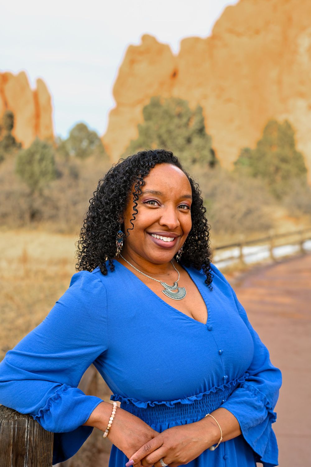 Woman in blue dress smiles while posing against sandstone formations at Garden of the Gods park in Colorado.