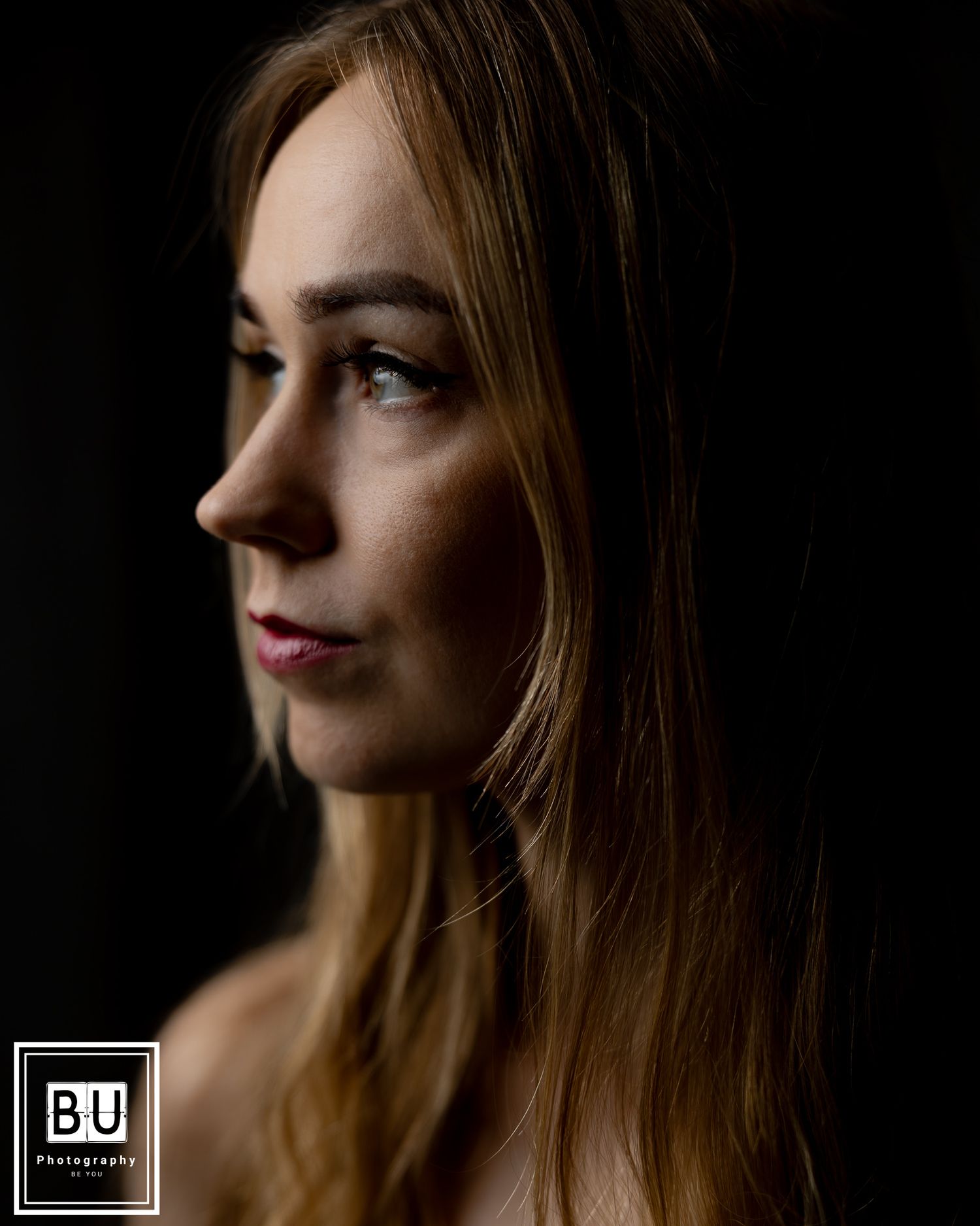 A side profile portrait against a dark background showcasing dramatic lighting and blonde hair.