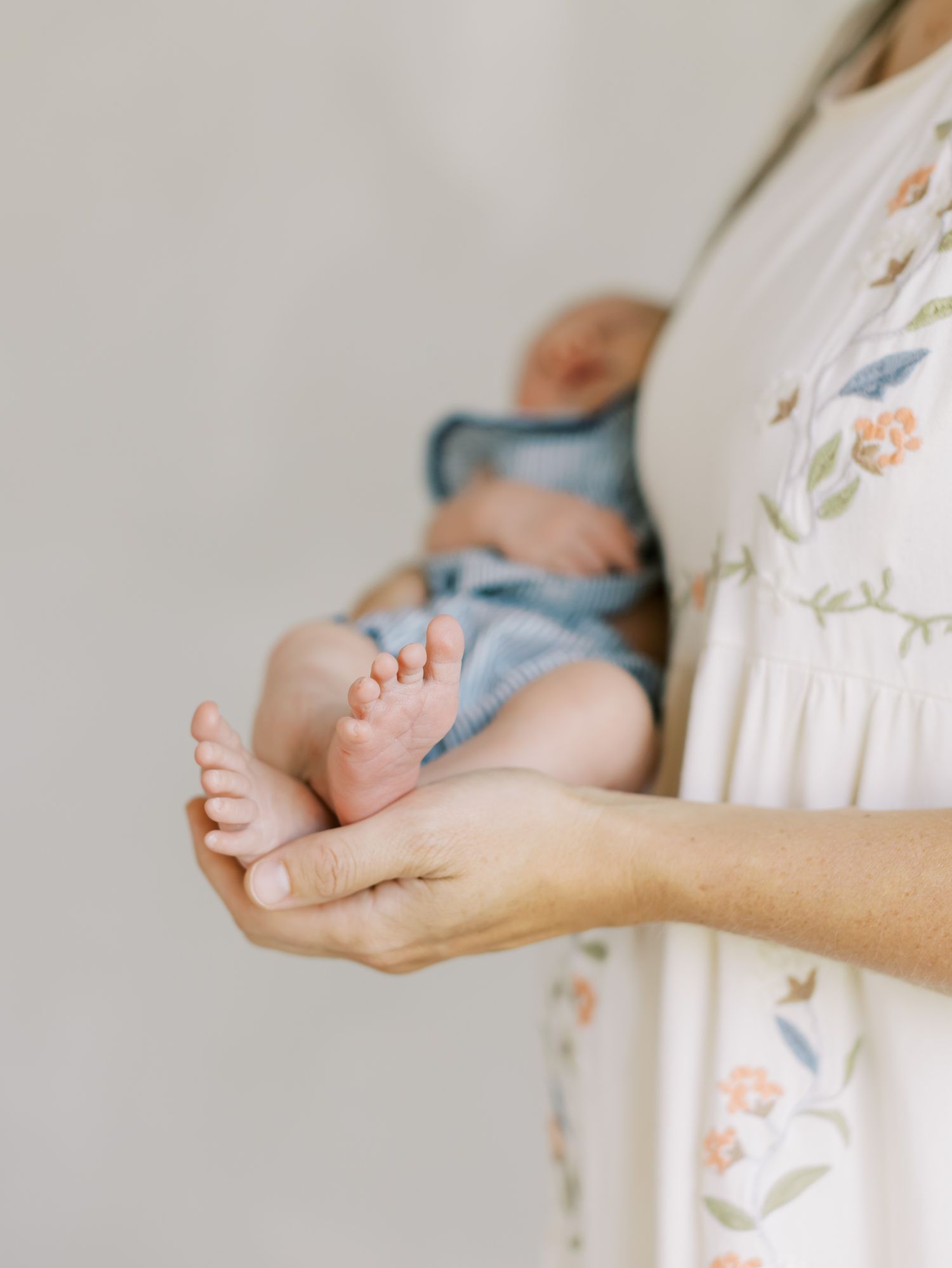 Tiny baby feet resting in gentle hands against a floral dress background.
