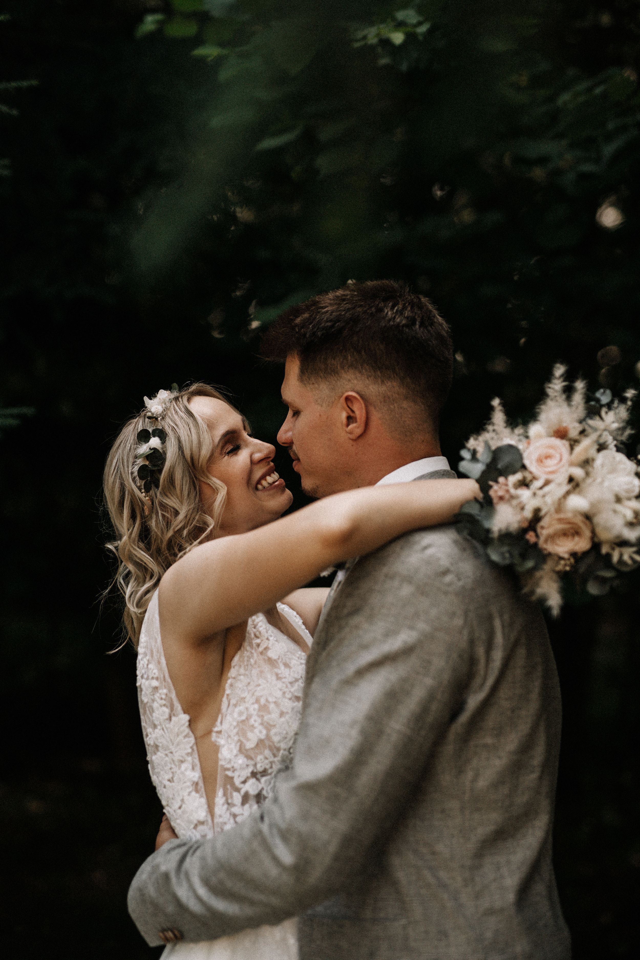 A romantic wedding portrait showing a tender embrace between newlyweds with delicate floral bouquet details.